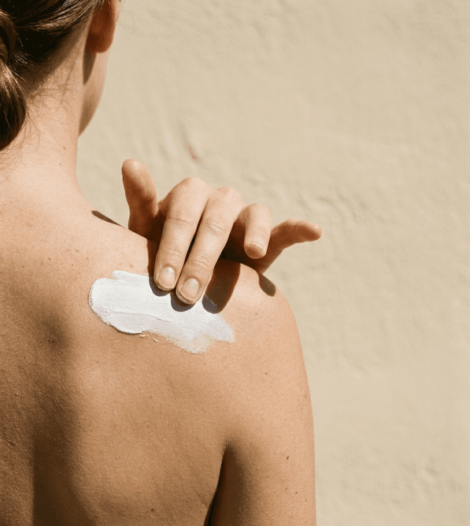 A hand pressing a flat smear of white zinc balm into a bare shoulder in hard midday sunlight